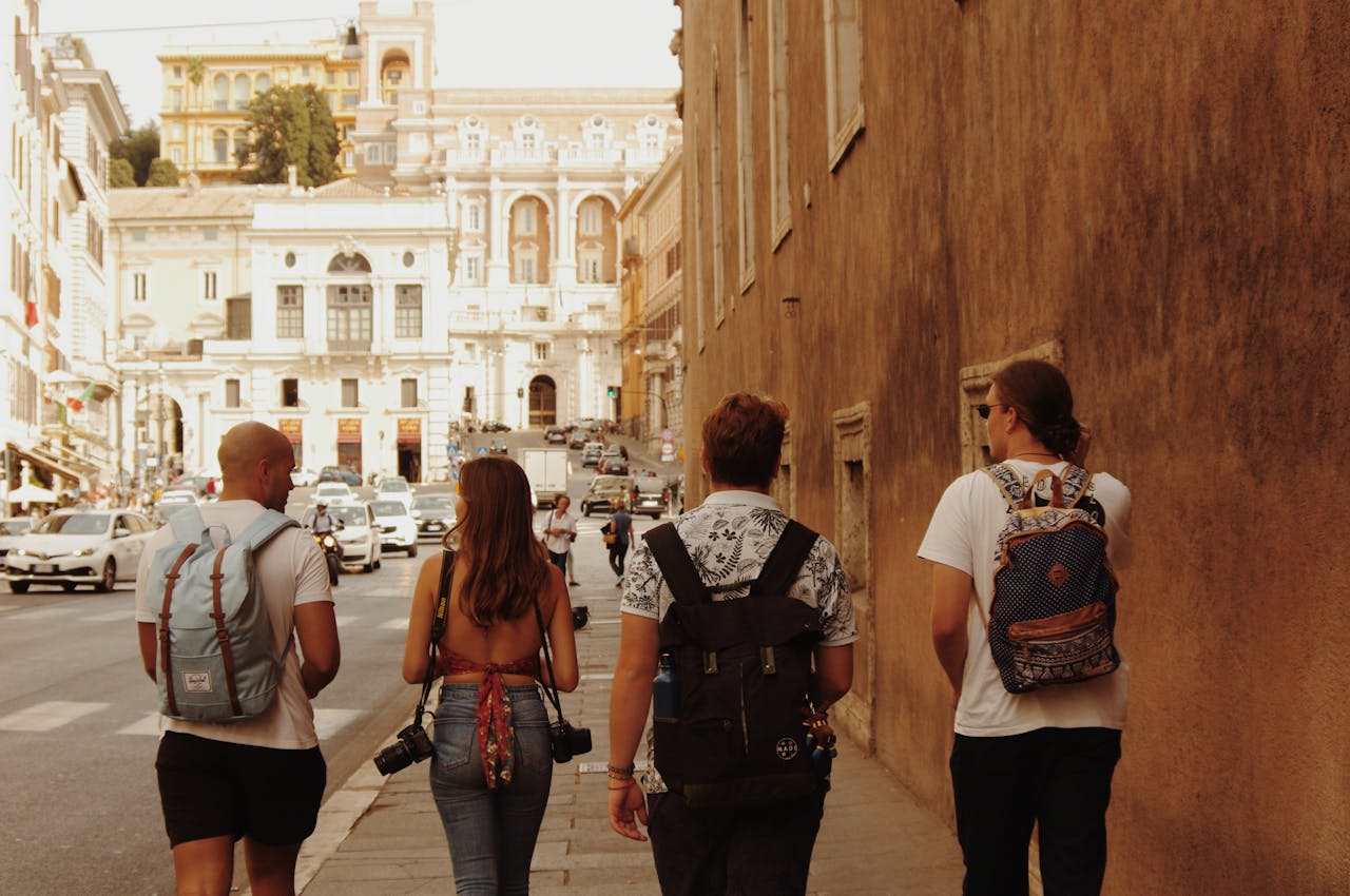 about-02 Four tourists with backpacks walking on a street in Rome, Italy, with historic architecture around.