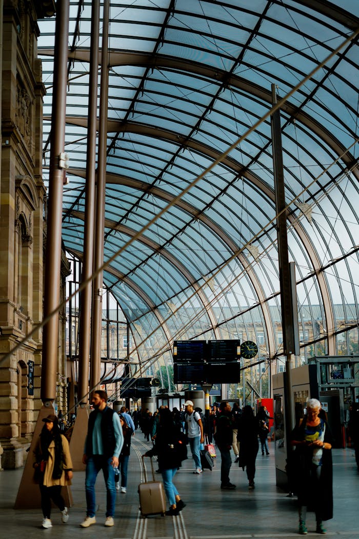 services-03 Travelers walking under a modern glass ceiling in a busy train station, showcasing urban transit life.