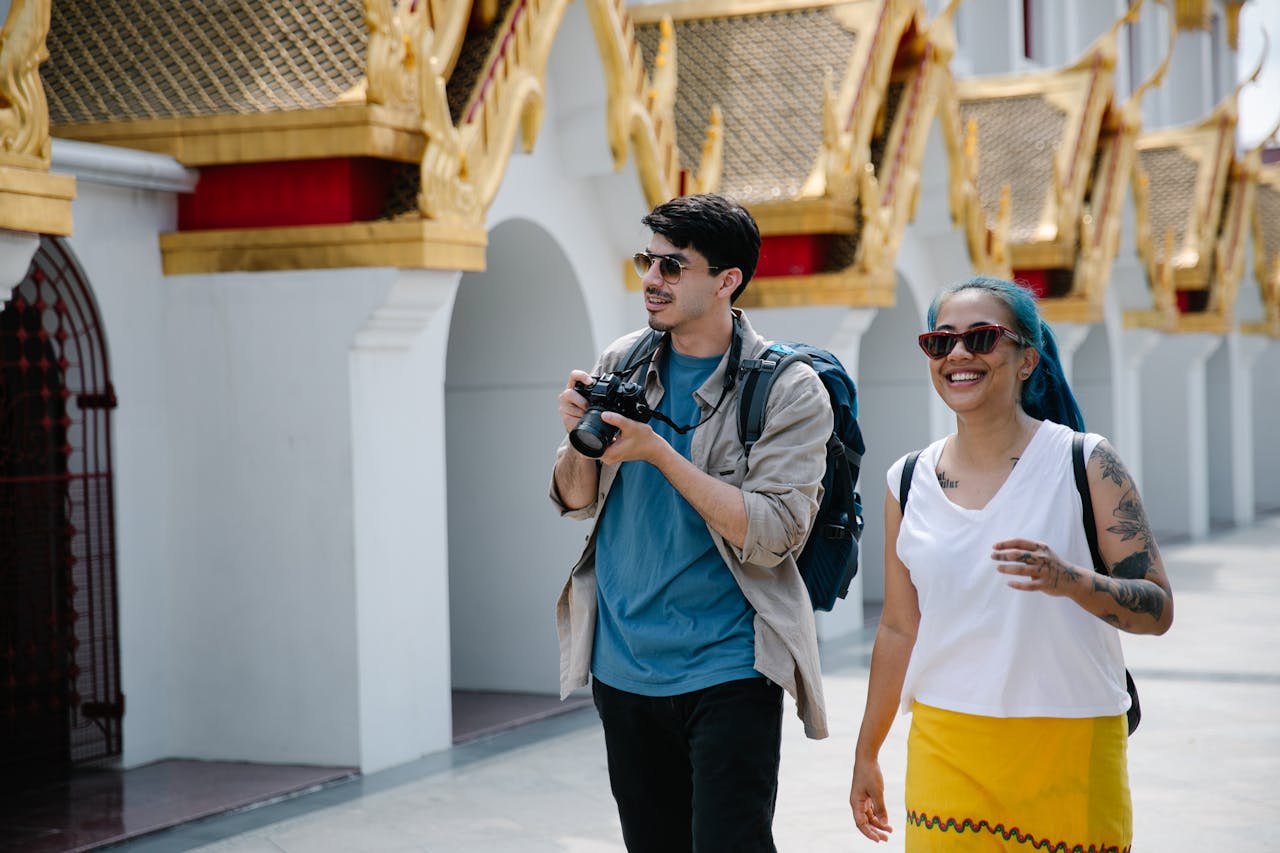 about-03 Two tourists with backpacks and cameras enjoy a sunny day exploring ornate Thai architecture.